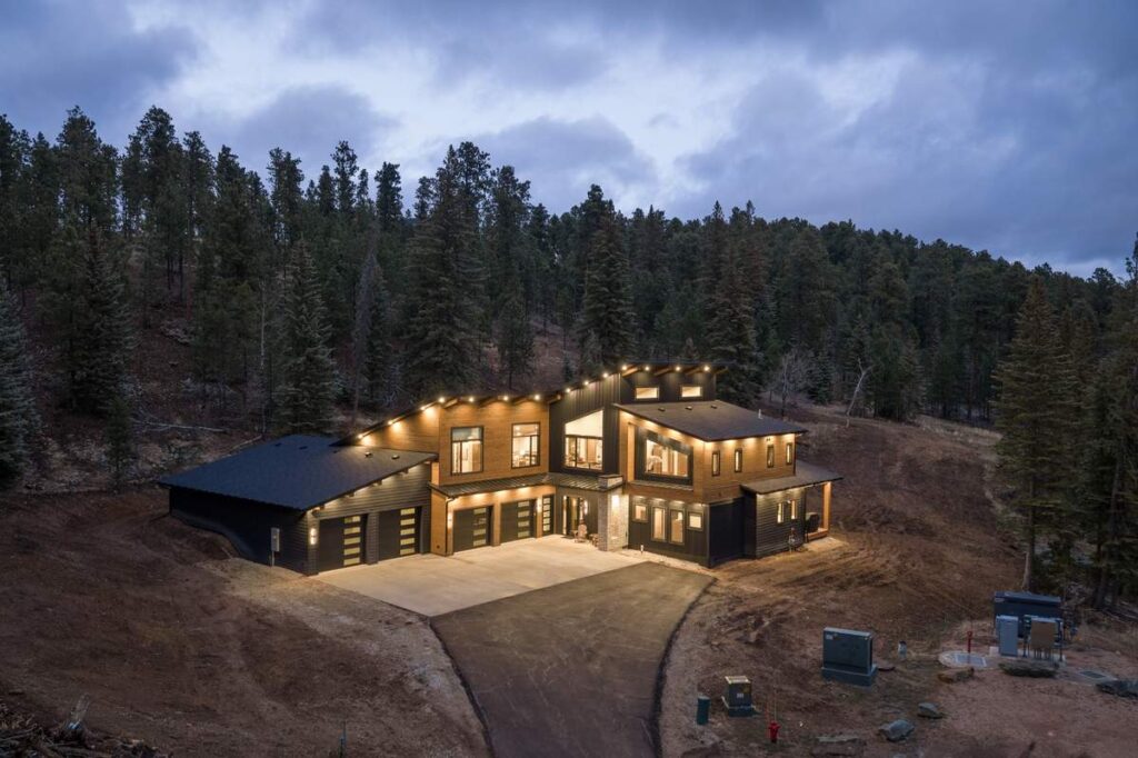 Back exterior of luxury home with covered patio, lighting, and forest surroundings